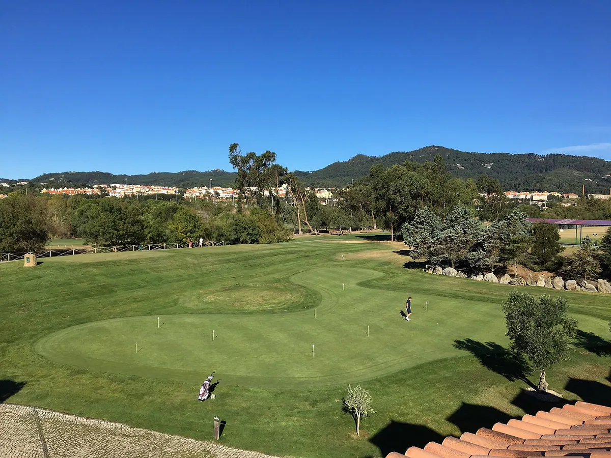 A green at Pestana Beloura Golf with golfers and the Sintra hills behind