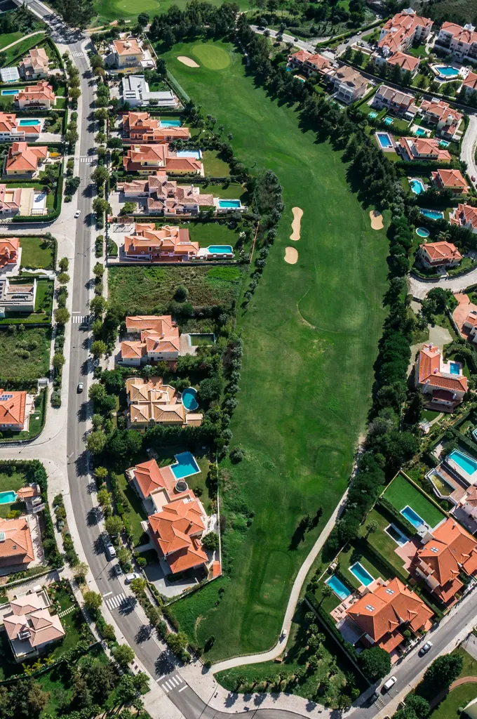 Aerial view of a Beloura street lined with villas, gardens and pools beside the golf course
