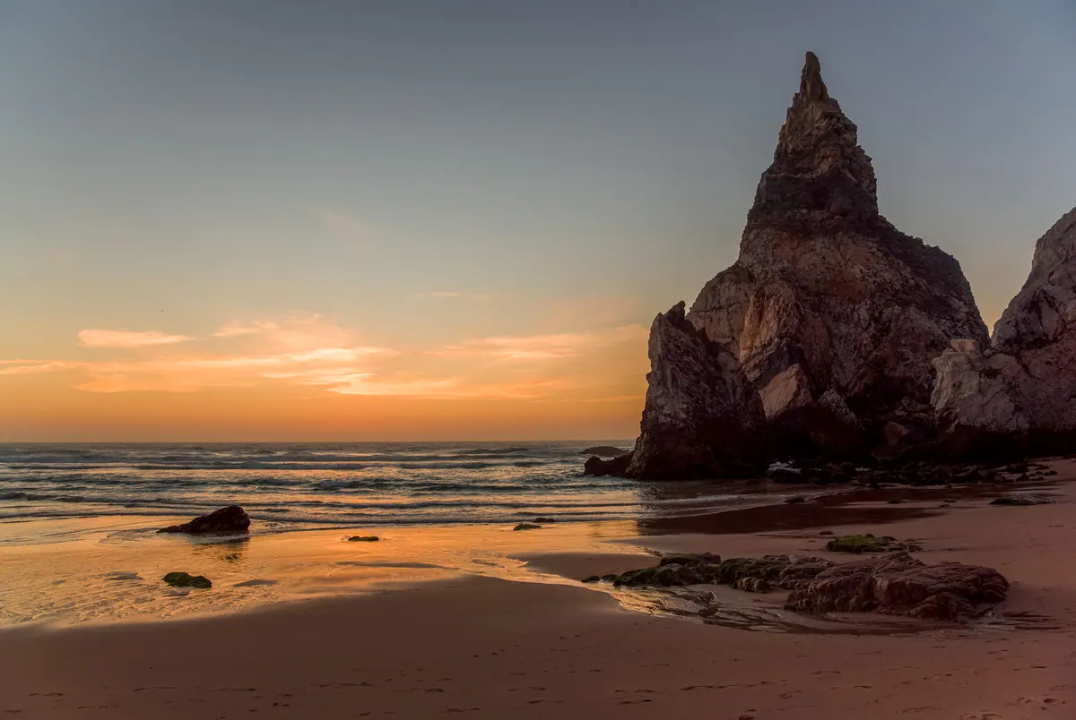 Praia da Ursa’s sea stack silhouetted against an orange sunset